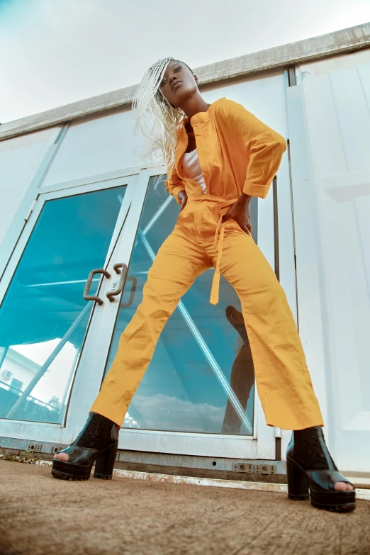 a woman in a yellow jumpsuit and black boots, by Nina Hamnett, trending on pexels, happening, in front of a garage, offwhite, orange, blonde