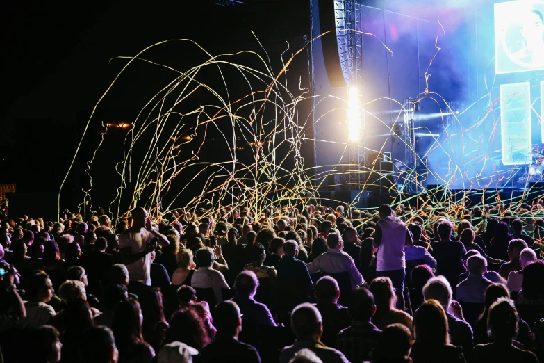 a large group of people standing in front of a stage, glow sticks, sparks and thunders, festivals, glowing epicentre