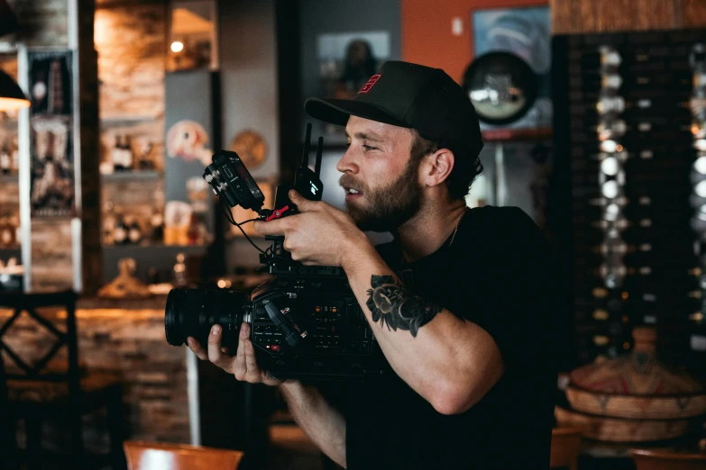 a man sitting at a table with a camera in front of him, red cinema camera, portrait featured on unsplash, avatar image, 2 4 0 p footage