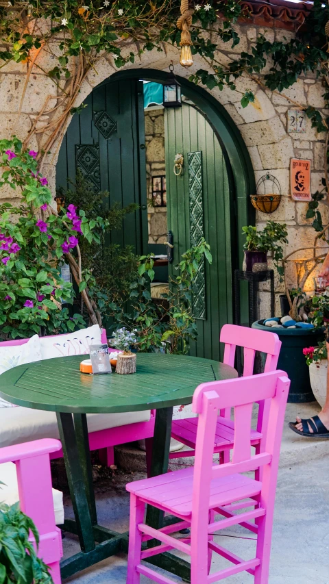 a patio with a green table and pink chairs, inspired by Riad Beyrouti, pexels contest winner, greek ameera al taweel, village house, brightly coloured hair, cafe