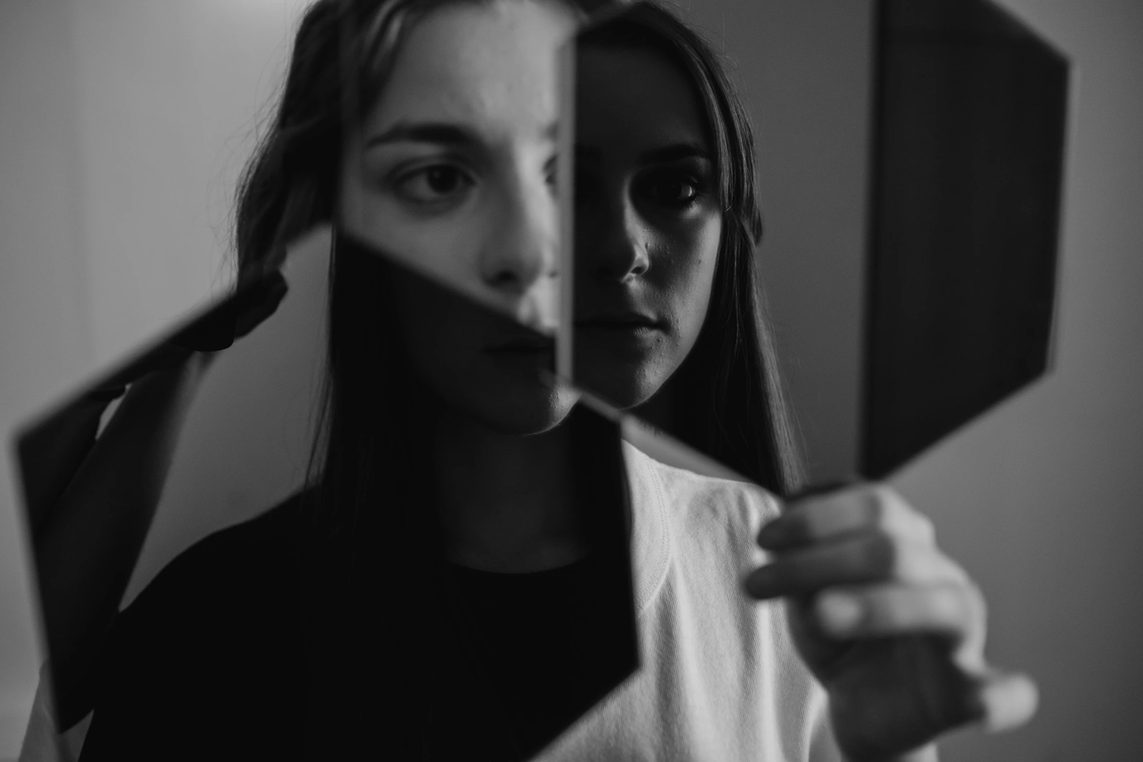 a woman holding a mirror in front of her face, a black and white photo, by Emma Andijewska, pexels contest winner, broken mirrors composition, image split in half, portrait of white teenage girl, 4k symmetrical portrait
