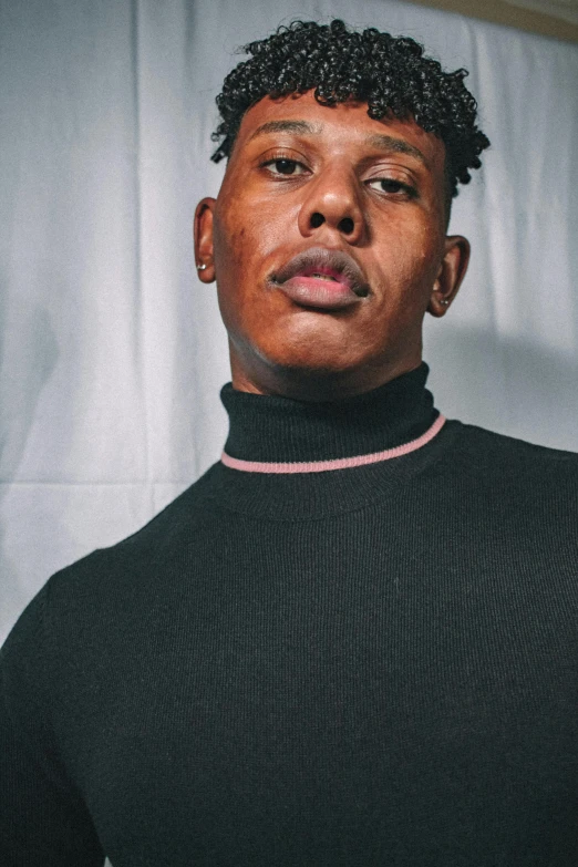 a man standing in front of a white curtain, an album cover, by Charles Martin, trending on pexels, realism, black turtle neck shirt, non binary model, headshot profile picture, wearing a sweater