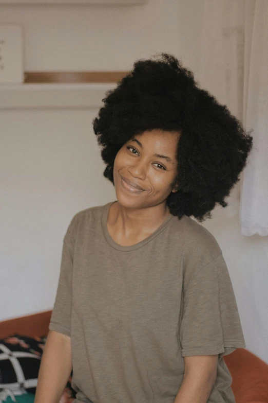 a woman with an afro sitting on a bed, a portrait, pexels contest winner, shoulder-length black hair, loosely cropped, smiling confidently, bedhead