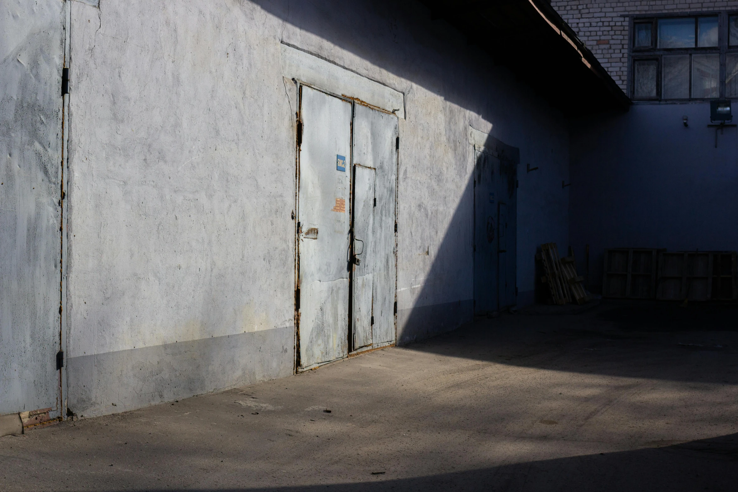 a man riding a skateboard up the side of a building, an album cover, by Attila Meszlenyi, arbeitsrat für kunst, abandoned car garage, blue door, volumetric light and shadow, rustic yet enormous scp (secure