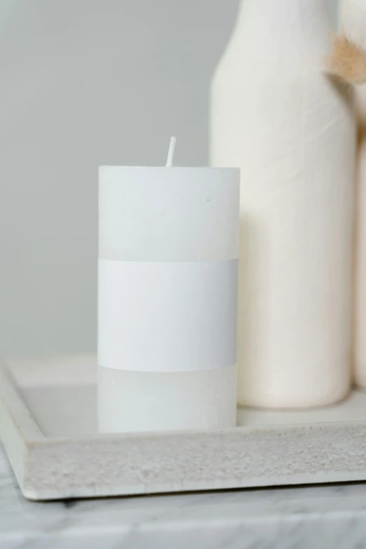 a white candle sitting on top of a tray, inspired by Rachel Whiteread, modern studio light soft colour, o'neill cylinder, trimmed with a white stripe, middle close up shot