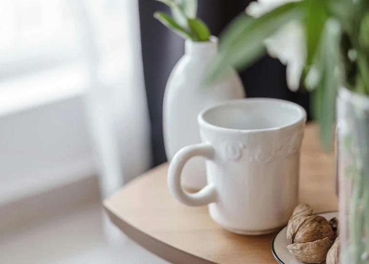 a white coffee cup sitting on top of a wooden table, a still life, inspired by Richmond Barthé, trending on pexels, soft window light, detail shot, white, with small object details