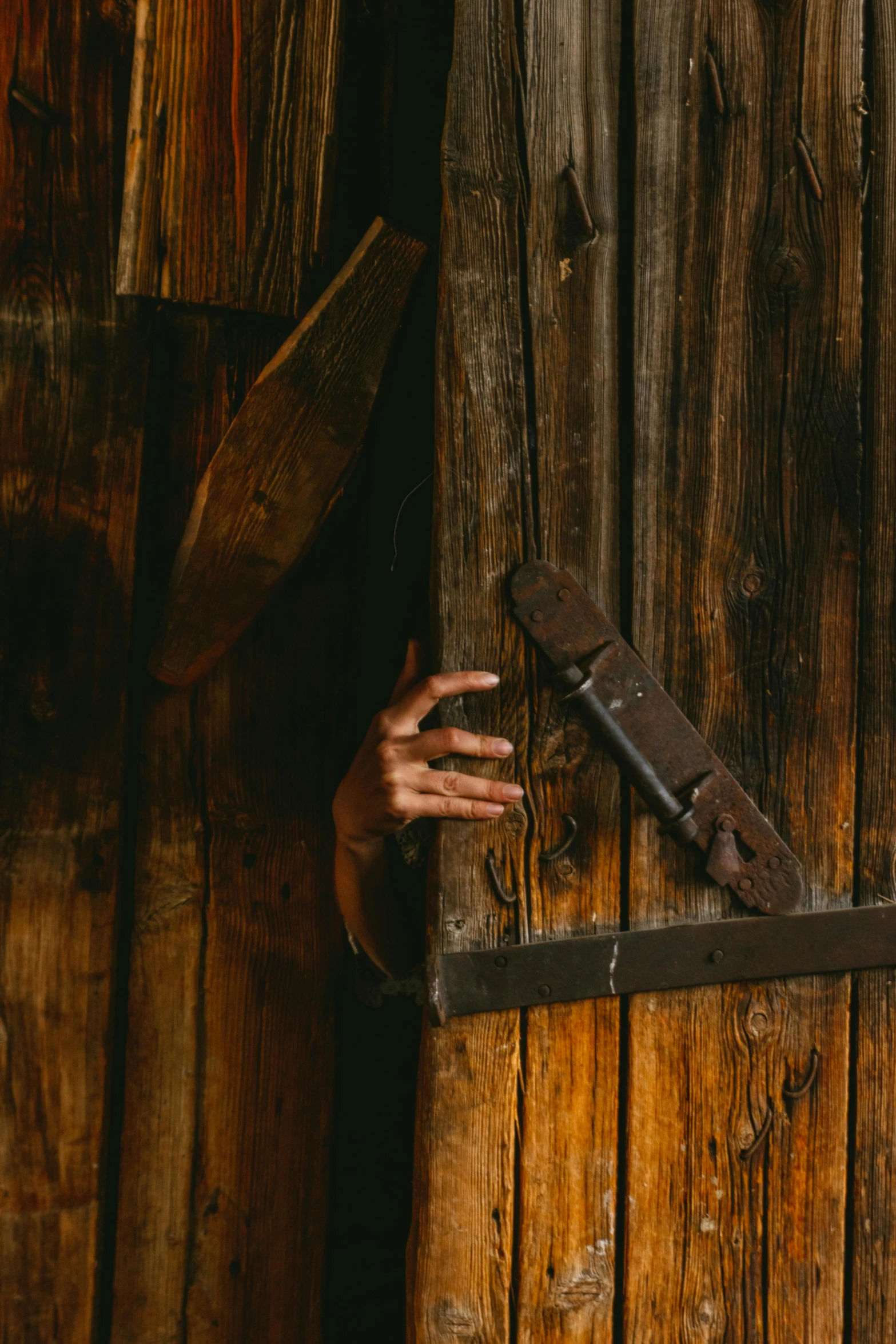 a woman standing in front of a wooden door, inspired by Elsa Bleda, pexels contest winner, hand holding a knife, barn, scaring, full width