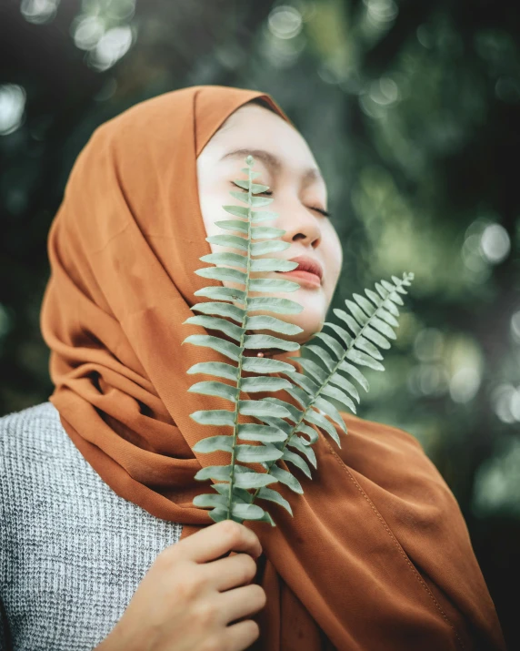 a woman in a hijab holding a fern leaf, inspired by Sasha Putrya, trending on pexels, cinnamon skin color, photo of slim girl, aestheticly inspired, staring at you