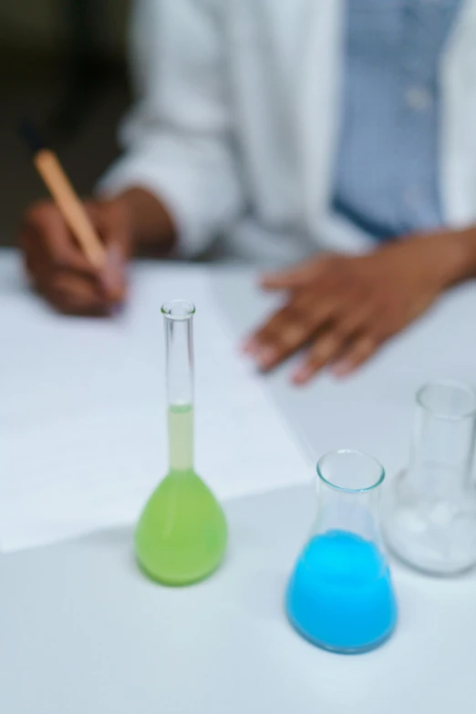 a woman in a lab coat writing on a piece of paper, analytical art, brand colours are green and blue, beakers, papers on table, promo image