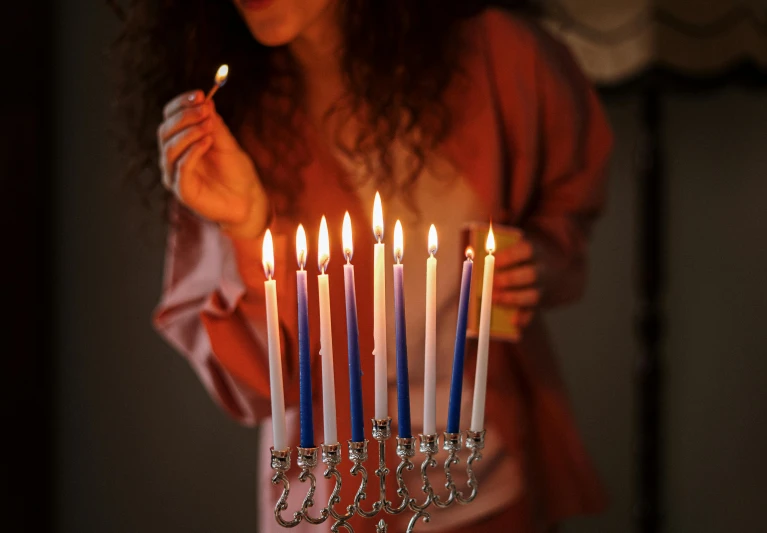 a woman blowing out candles on a menorah, pexels, fine art, light red and deep blue mood, silver accessories, a person standing in front of a, hebrew