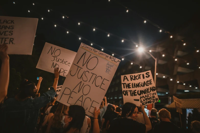 a group of people holding up signs at a protest, by Julia Pishtar, trending on unsplash, summer night, background image