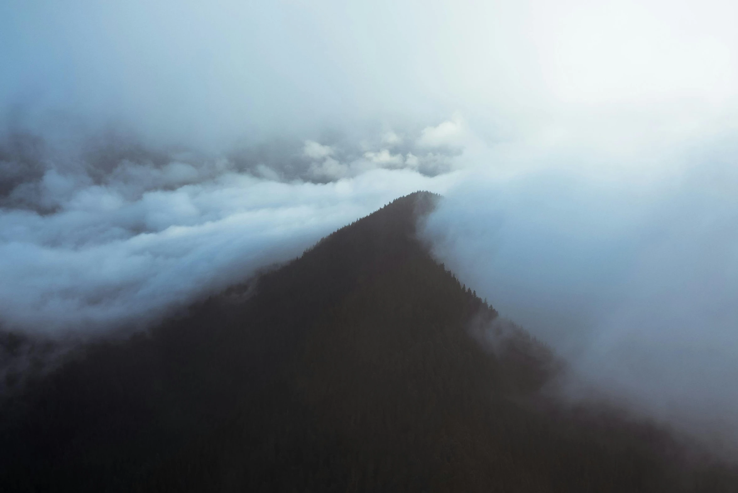 a view of a mountain covered in clouds, pexels contest winner, minimalism, ominous! landscape of north bend, drone photo, foggy volumetric lighting, atmospheric”