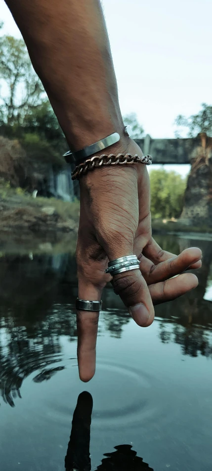 a close up of a person's hand near a body of water, inspired by L. A. Ring, renaissance, metal neck rings, aboriginal, in a post apocalyptic setting, in a row