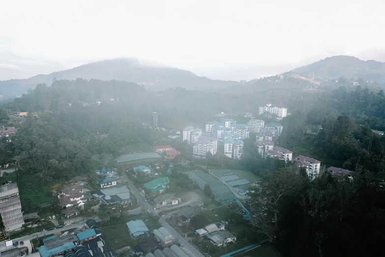 an aerial view of a city with mountains in the background, an album cover, by Basuki Abdullah, unsplash, hurufiyya, foggy day, hideen village in the forest, residential area, slightly pixelated