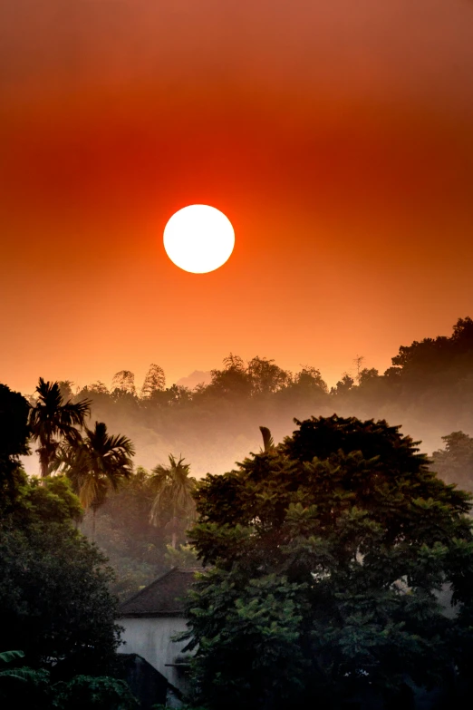 the sun is setting over the trees and buildings, a picture, inspired by Steve McCurry, sumatraism, orange, laos, big red sun, landscape photo