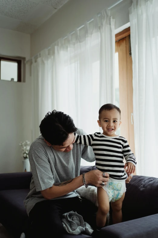 a man sitting on top of a couch next to a little boy, by Basuki Abdullah, pexels contest winner, diaper-shaped, boy has short black hair, gif, standing