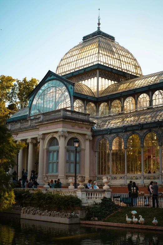 a large building sitting next to a body of water, inspired by Luis Paret y Alcazar, art nouveau, greenhouse, during autumn, neoclassical, in the evening