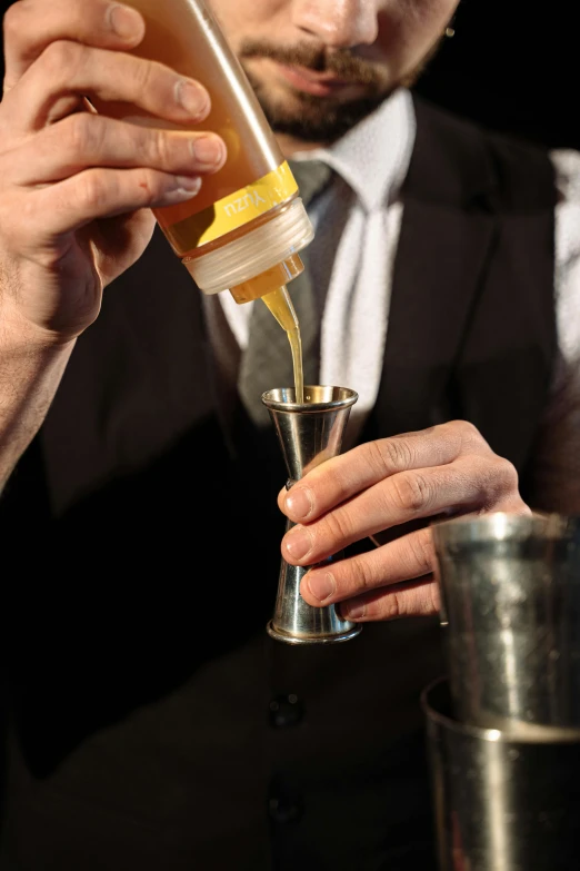 a man in a suit pouring something into a glass, silver and yellow color scheme, pictured from the shoulders up, bar, syrup
