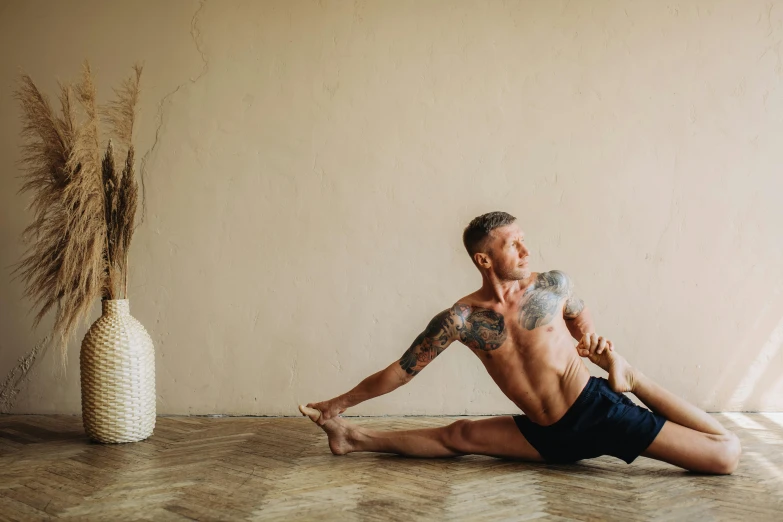 a man sitting on the floor doing a yoga pose, a portrait, by Matija Jama, pexels contest winner, athletic body, man holding spear, serpentine pose, natural light in room