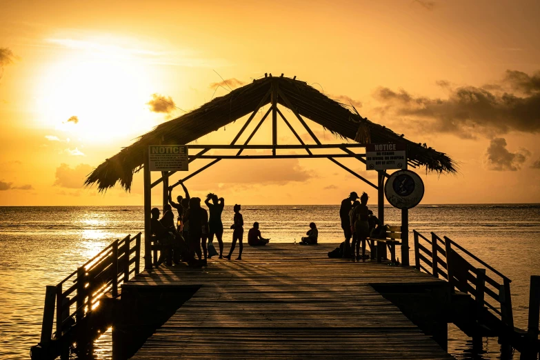 a group of people standing on a pier at sunset, by Carey Morris, pexels contest winner, jamaican vibe, wooden structures, thumbnail, clear and sunny