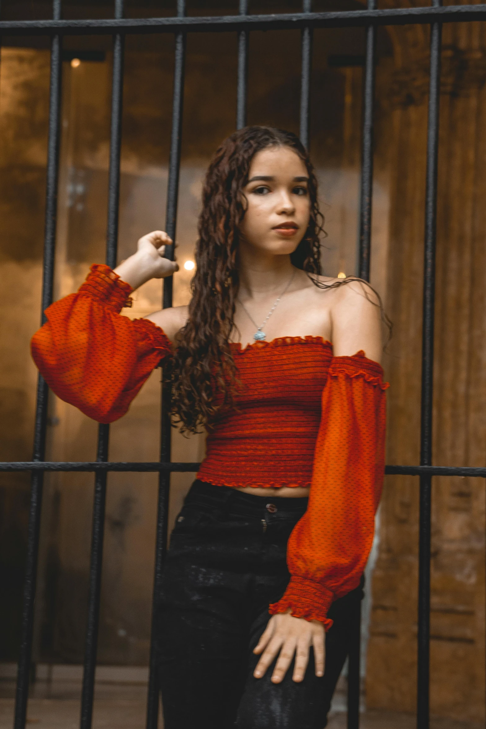 a woman standing in front of a jail cell, an album cover, inspired by Elsa Bleda, trending on pexels, renaissance, madison beer girl portrait, red shirt, liberty curls, girl under lantern