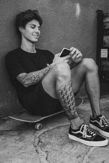 a black and white photo of a man sitting on a skateboard, a tattoo, inspired by Seb McKinnon, gray shorts and black socks, he is holding a smartphone, androgynous person, dimples