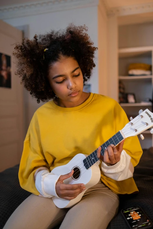 a woman sitting on a couch playing a guitar, holding a yellow toothbrush, black teenage girl, 2019 trending photo, ukulele