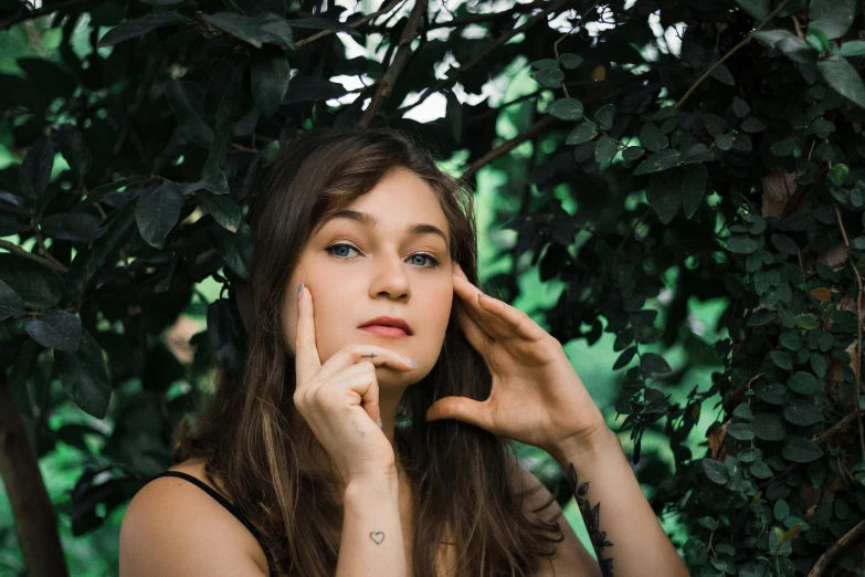 a beautiful young woman holding her hand to her face, inspired by Elsa Bleda, trending on pexels, trees in the background, portrait image, low quality photo, girl with brown hair