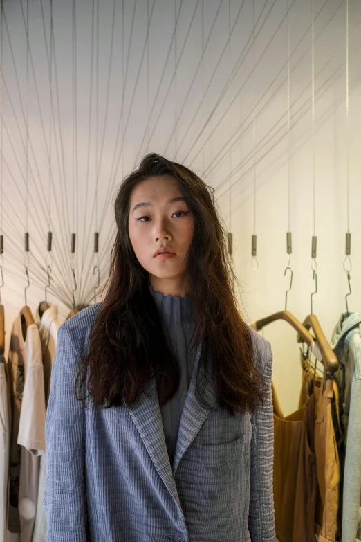 a woman standing in front of a rack of clothes, inspired by Kim Tschang Yeul, grey jacket, pictured from the shoulders up, portrait n - 9, architect