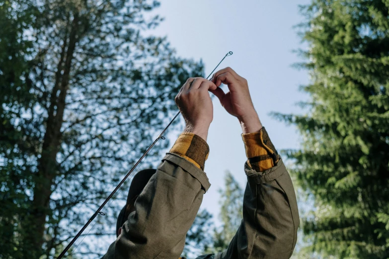 a man that is flying a kite in the air, by Emma Andijewska, unsplash, process art, fishing pole, forest details, holding flask in hand, detailed product shot