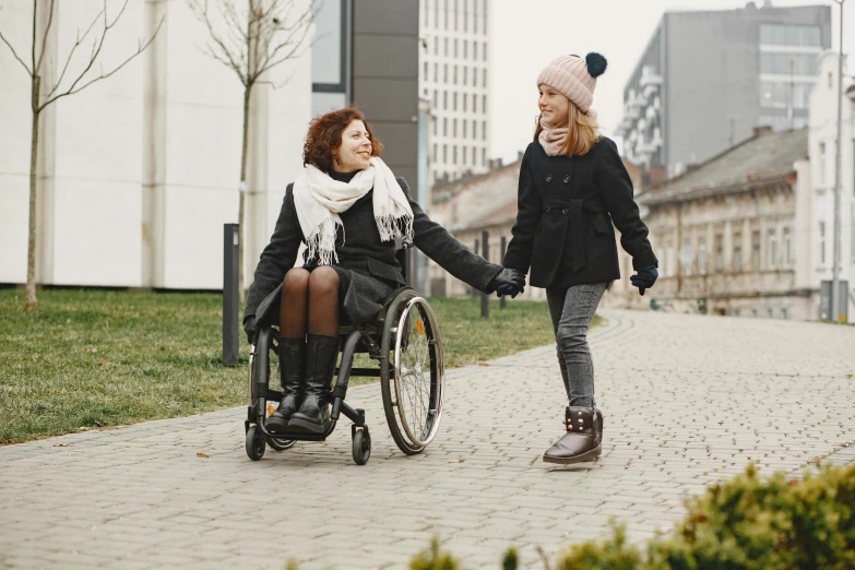 a woman pushing a woman in a wheelchair down a sidewalk, a portrait, trending on pexels, hurufiyya, winter season, thumbnail, beautiful girl, holding hands