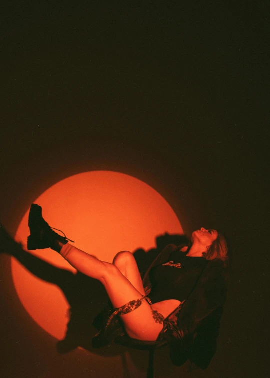 a woman on a pole with the sun in the background, an album cover, inspired by Elsa Bleda, trending on unsplash, sitting on the floor, red moon, black and orange, dark. studio lighting