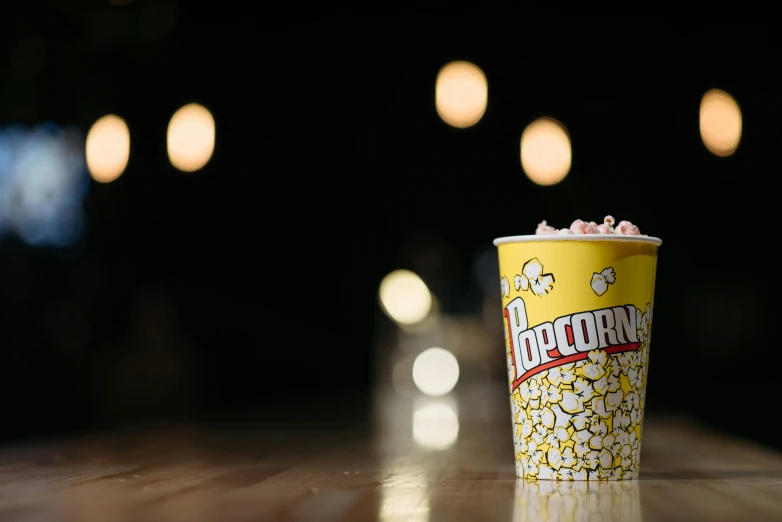 a popcorn cup sitting on top of a wooden table, profile image, background image, it's night time, advertising photo