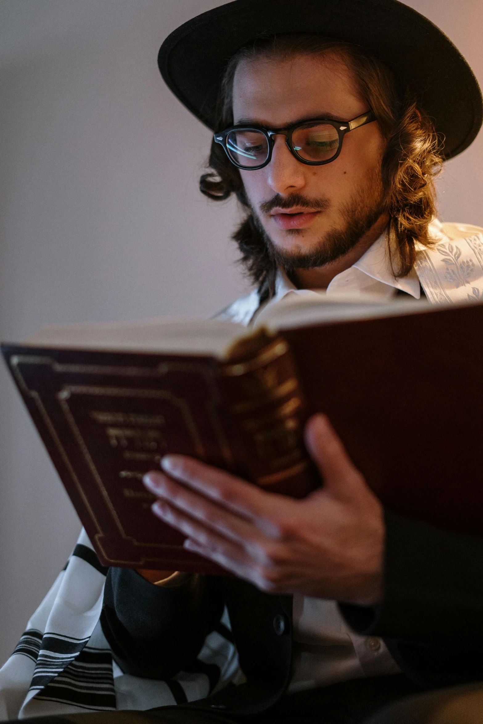 a man in a hat reading a book, by Leo Michelson, trending on unsplash, renaissance, jewish young man with glasses, dressed as an oracle, taken in the late 2010s, wearing fancy clothes