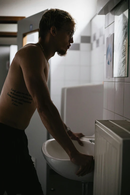 a man standing next to a urinal in a bathroom, a tattoo, unsplash, process art, in a kitchen, indigenous man, thin young male, ignant