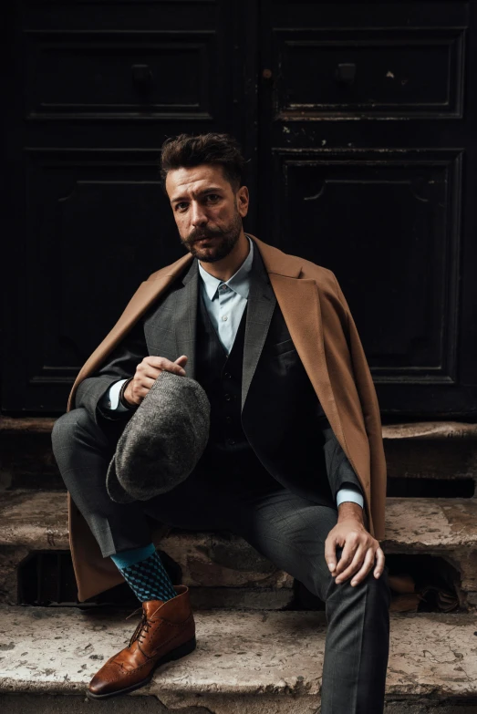 a man sitting on the steps of a building, a portrait, inspired by Salomon van Abbé, pexels contest winner, renaissance, trench coat and suit, shia labeouf, caramel. rugged, black stetson and coat