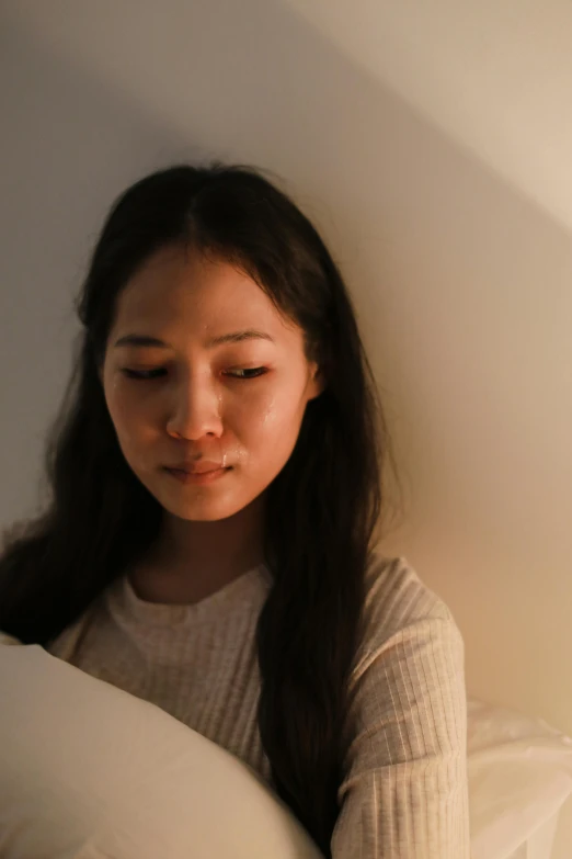 a woman sitting on a bed reading a book, by helen huang, sad lighting, south east asian with round face, exhausted face close up, wide forehead