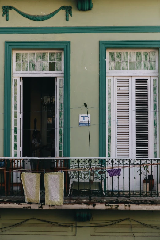 a balcony with clothes hanging out of it, an album cover, by Emanuel Witz, flickr, 30-year-old woman from cuba, green and blue color scheme, view from across the street, symmetrical doorway