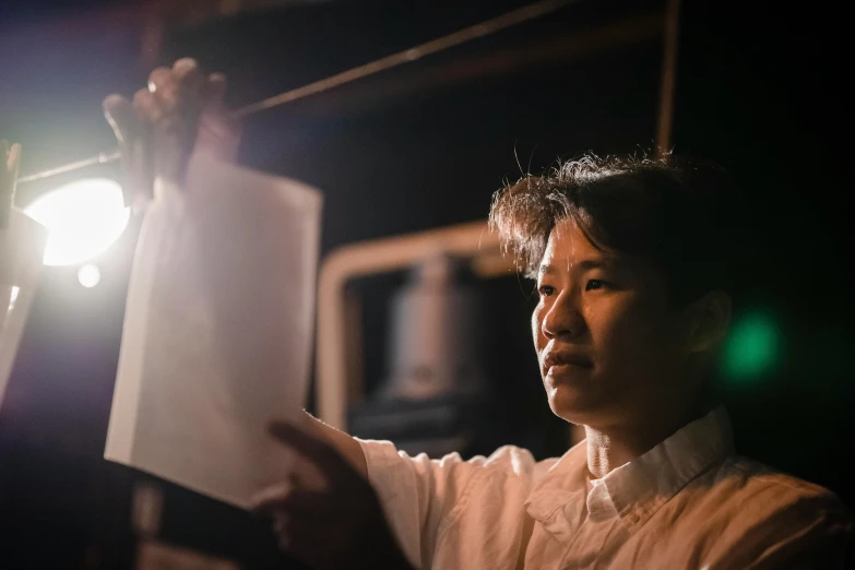 a close up of a person holding a light, a portrait, inspired by Yukimasa Ida, pexels contest winner, in a kitchen, engineer, standing in a dimly lit room, he is holding a large book