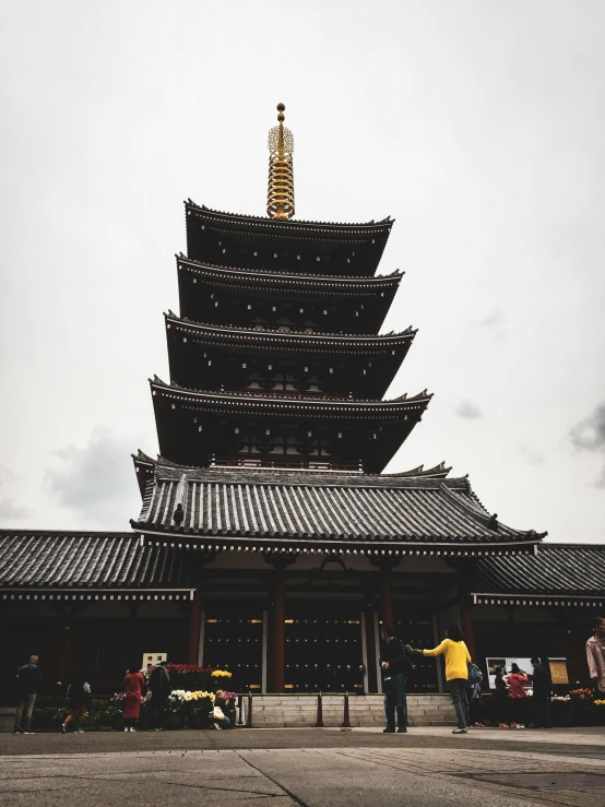 a group of people standing in front of a pagoda, inspired by Itō Jakuchū, pexels contest winner, buildings covered in black tar, view from ground, slight overcast lighting, lead - covered spire