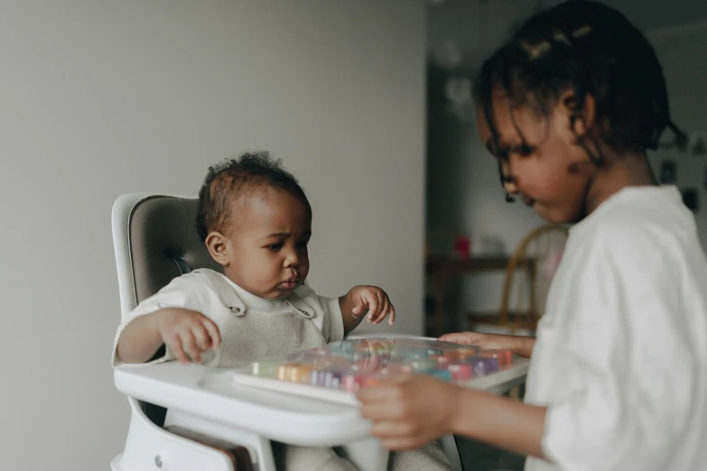 a little girl that is sitting in a high chair, pexels contest winner, close together, dark-skinned, working hard, without duplicate image