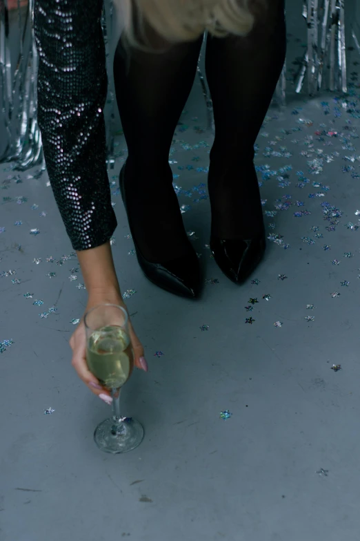 a close up of a person holding a wine glass, happening, feet on the ground, champagne, black and silver, wearing festive clothing