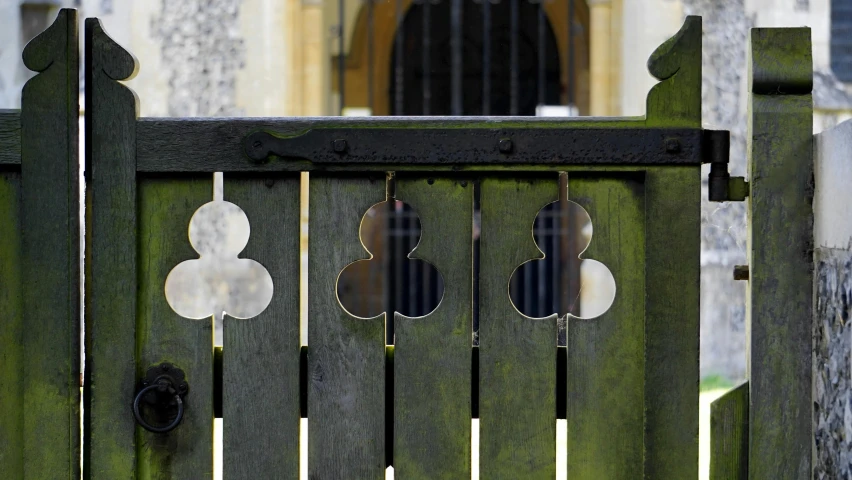 a close up of a gate with a building in the background, inspired by Robert Bevan, unsplash, arts and crafts movement, rorschach, question marks, a wooden, chrome cathedrals