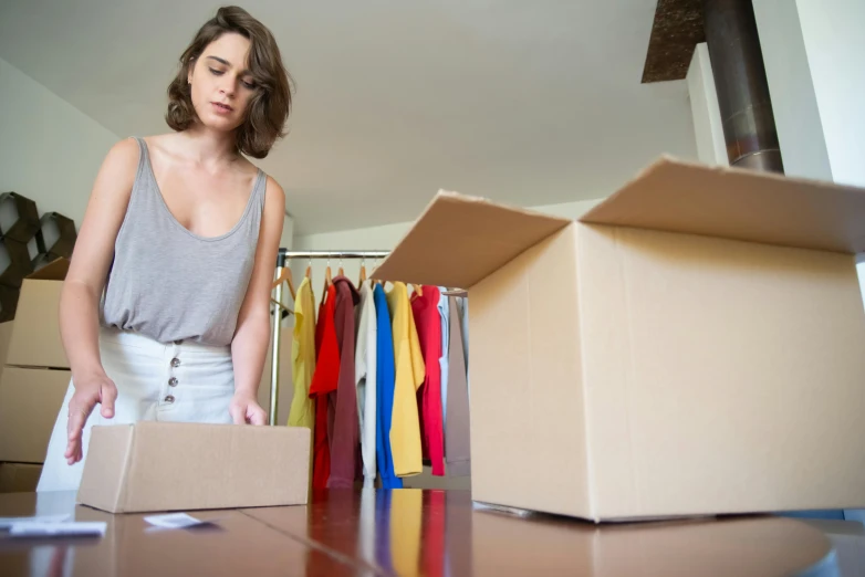 a woman standing in front of a cardboard box, leaving a room, looking sad, avatar image, ecommerce photograph