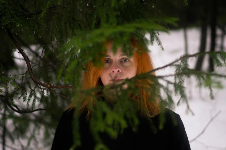 a woman standing next to a tree in the snow, an album cover, inspired by Louisa Matthíasdóttir, pexels contest winner, renaissance, orange hair, portrait close - up, black fir, production still