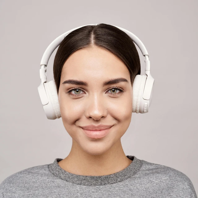 a woman wearing headphones and smiling at the camera, trending on pexels, on a gray background, with symmetrical facial features, technological, sleek white