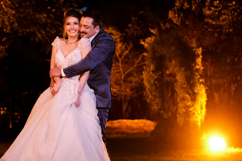 a man and a woman standing next to each other, by Arthur Sarkissian, pexels contest winner, romanticism, fireball lighting her face, with a tree in the background, bride and groom, greek ameera al taweel