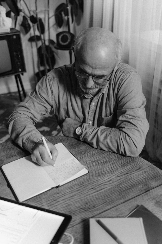 a man sitting at a table writing in a book, a black and white photo, by István Árkossy, eric carle, digital image, holding notebook, (pen)