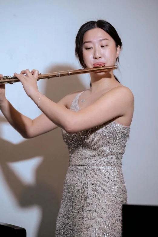 a woman in a silver dress playing a flute, inspired by Zheng Xie, unsplash, low quality photo, yanjun chengt, david luong, smol