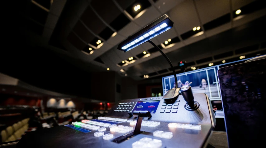 a computer monitor sitting on top of a desk, video art, theatre equipment, dramatic white and blue lighting, controls, inside a grand studio